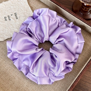 Close-up of a large purple satin hair scrunchie with ruffled edges on a beige tray