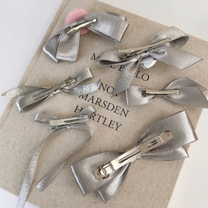 Set of six silver silk-textured bow hair clips in various styles on beige background