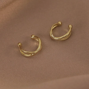 Détail de boucles d'oreilles croisées dorées à double couche sur fond de soie élégante