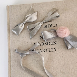 Detail of silver metallic bow hair clips with pink chiffon rose on linen background