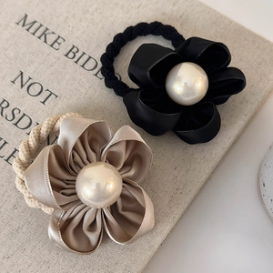 Close-up of satin camellia hair ties with large pearls in black and champagne gold