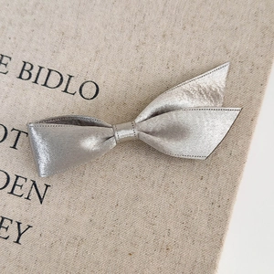 Close-up of a silver satin ribbon bow hair clip on a textured linen fabric background