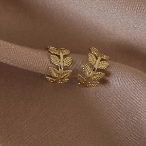 Vue macro détaillée de boucles d'oreilles feuilles dorées sur soie champagne