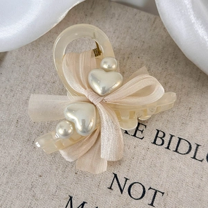 Detailed shot of cream resin hair claw clip with chiffon bow and pearl heart accents