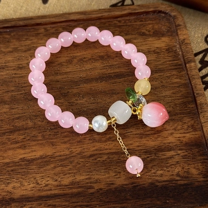Gros plan d'un bracelet à breloque pêche avec perles œil de chat sur plateau bois