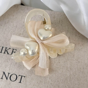 Close-up of cream hair claw clip with elegant beige bow and heart pearl accents