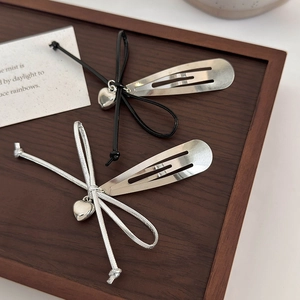Détail de pinces à cheveux argentées avec nœuds tissés et pendentifs en forme de cœur
