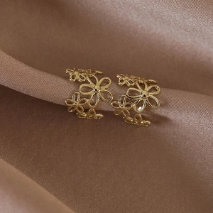 Gros plan d'un ear cuff fleuri doré sur tissu en soie marron au design ajouré