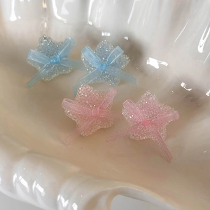 Macro shot of sugar-textured star earrings with pink and blue ribbons on a seashell tray