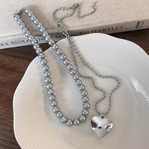 Ensemble collier avec pendentif cœur argenté et perles grises sur une assiette blanche