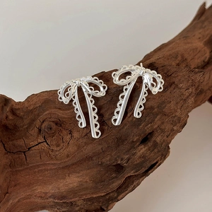 Minimalist silver ribbon bow earrings with lace hollow design on natural wood base