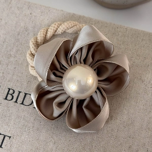 Detailed macro view of champagne satin camellia flower hair tie with white pearl center