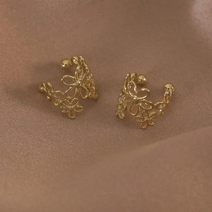Gros plan d'un ear cuff fleuri doré posé sur un tissu en satin marron élégant