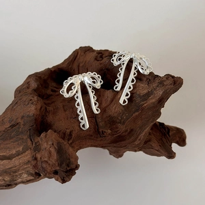 Minimalist silver ribbon bow earrings with hollow lace design on wood background
