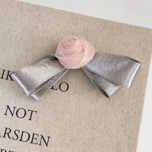 Detail of pink mesh rose and silver satin ribbon bow hair clip on a textured background