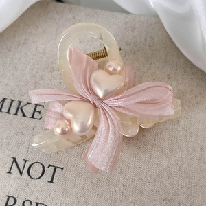 Close-up of cream resin hair claw clip with pink silk bow and heart pearl details