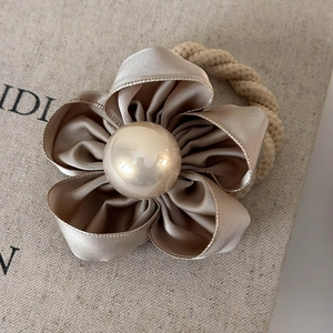 Close-up of elegant champagne satin camellia hair tie with a large pearl center piece