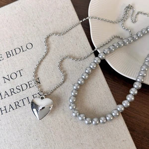 Détail du collier double rang avec pendentif cœur poli et chaîne de perles grises élégante
