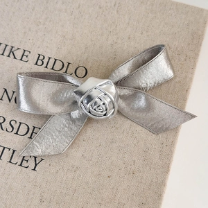 Close-up of a silver bow hair clip with a 3D rose flower on vintage book background