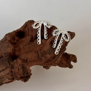 Close-up of silver bow earrings with hollow lace texture on natural wood display