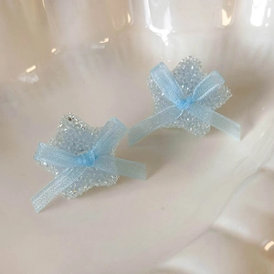 Detailed view of light blue star earrings with a small ribbon bow and crystal texture