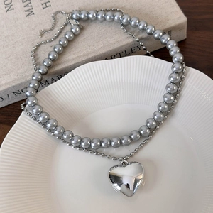 Gros plan d'un collier double rang en perles avec pendentif cœur argenté sur assiette