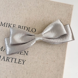 Close-up of metallic silver double-layer bow hair clip with fine satin texture on fabric