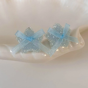 Close-up of light blue star earrings with glittery texture and small ribbon bows