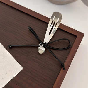 Détail de la pince à cheveux argentée avec nœud noir et pendentif cœur brillant