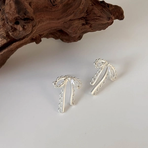 Close-up of silver ribbon bow earrings featuring hollowed lace patterns and matte finish