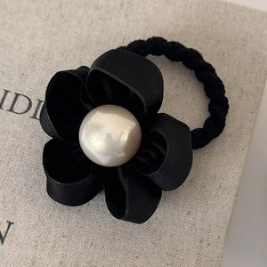 Detailed macro view of a black silk camellia hair tie with a large glossy white pearl
