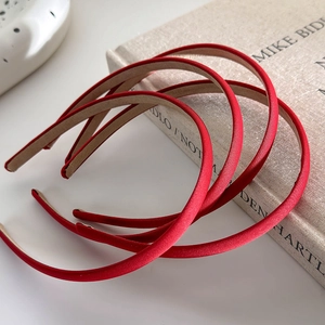 Close-up of three thin red satin headbands on a beige linen book with soft lighting