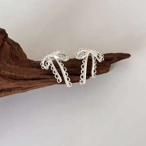 Minimalist silver ribbon bow earrings with lace hollow design on a vintage wood display