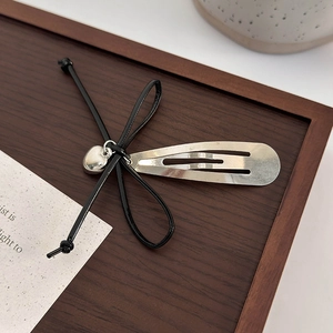 Détail d'une pince à cheveux avec nœud noir et pendentif cœur argenté sur bois