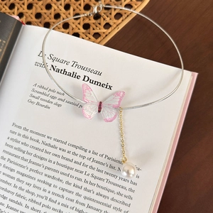 Détail d'un collier papillon vintage avec paillettes roses et perle blanche sur un livre
