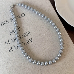 Détails du collier de perles grises avec fermoir métallique sur un tissu en lin épuré