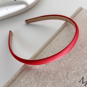 Detailed view of a slim red satin headband with a non-slip lining on a book