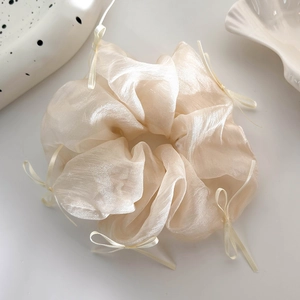 Dettaglio di un elastico per capelli in seta color crema con piccoli fiocchi decorativi