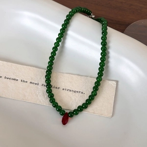 Vintage green beaded choker necklace featuring a red teardrop pendant on a ceramic dish
