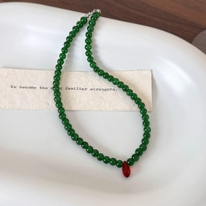 Vintage Chinese style green beaded necklace with red teardrop pendant on white tray
