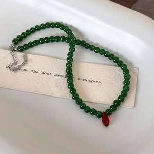 Macro shot of green beaded choker with a red teardrop pendant and silver chain detail