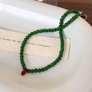 Detail of green beaded necklace with red teardrop pendant on a white ceramic plate