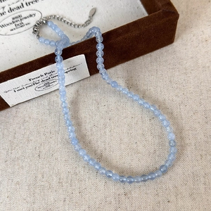 Detailed view of sea blue beaded necklace with silver lobster clasp on rustic fabric background
