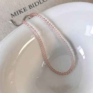 Close-up of a pink glass bead necklace with a silver extension chain on a ceramic bowl
