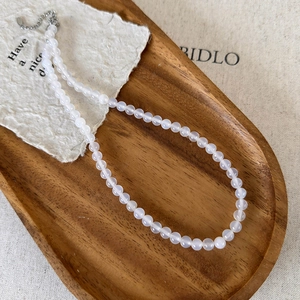 Detail of beaded white agate necklace featuring a silver lobster clasp on a wooden tray