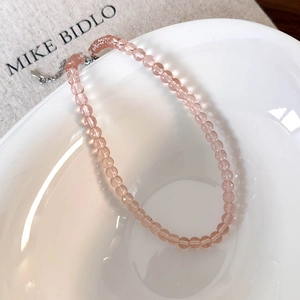 Detailed close-up of pink glass beaded necklace with silver chain in white ceramic bowl