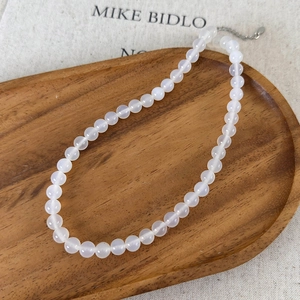 Detailed macro of white agate beaded necklace with silver lobster clasp on wooden tray