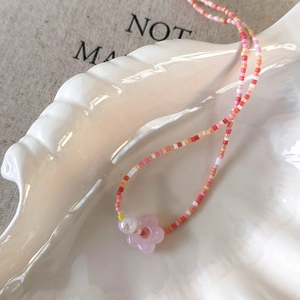 Detail view of colorful beaded floral necklace on a white shell ceramic jewelry tray