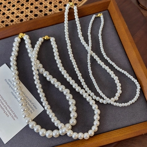 Detail view of round white pearl necklaces in two sizes with gold magnetic ball clasps