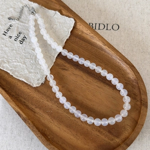 Macro shot of natural white agate beaded necklace with metal clasp on wooden tray